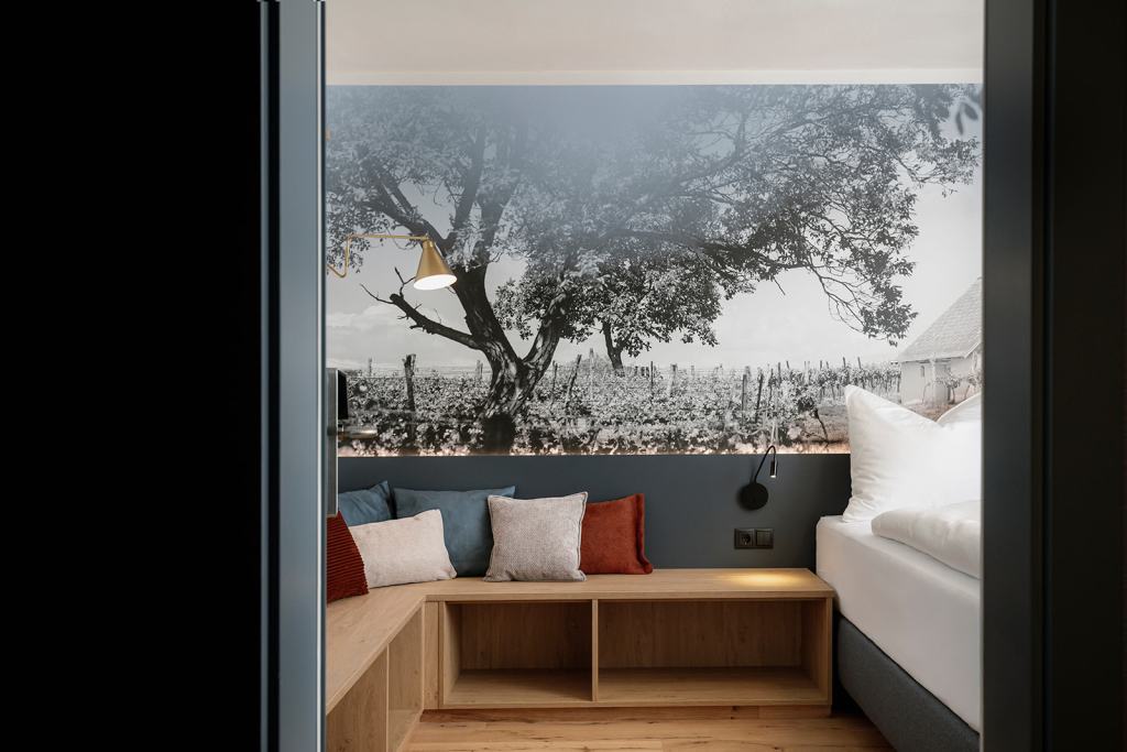 Schlafzimmer mit Doppelbett, gepolsterter Sitzbank und beleuchteter Fotowand mit Weingarten-Motiv im Zollquartier